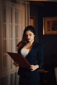 Young woman looking at file while standing at home