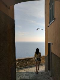 Rear view of woman walking by building against sea