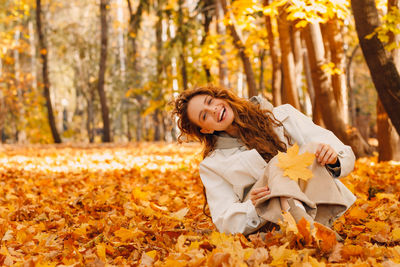 Portrait of young woman standing by tree trunk