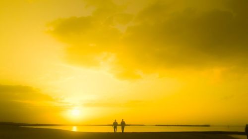 Silhouette people standing on sea against sky during sunset