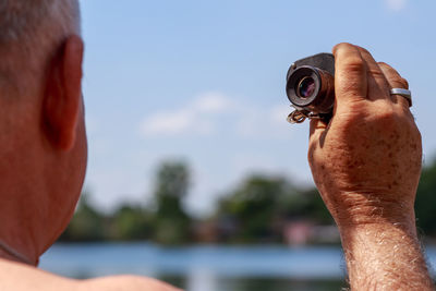 Close-up of man holding binoculars against sky