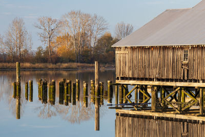 Wooden house by lake against sky