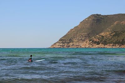 Rear view of man surfing in sea against clear sky