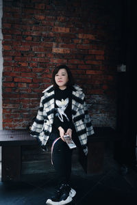 Portrait of young woman standing against brick wall