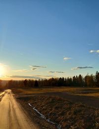 Road amidst field against sky during sunset