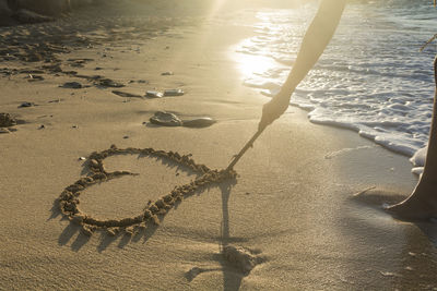 Close-up of person drawing heart on sand at beach