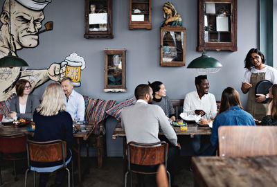 Owner talking to multi-ethnic friends while family having brunch at table in restaurant