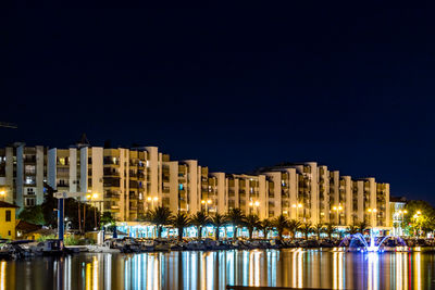 Illuminated buildings by river against sky at night