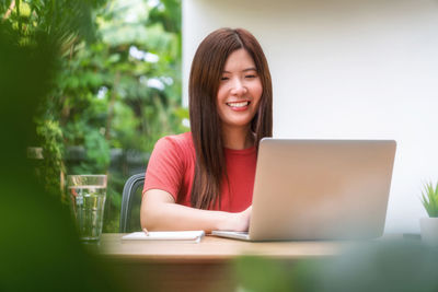 Portrait of smiling young woman using phone while sitting on table