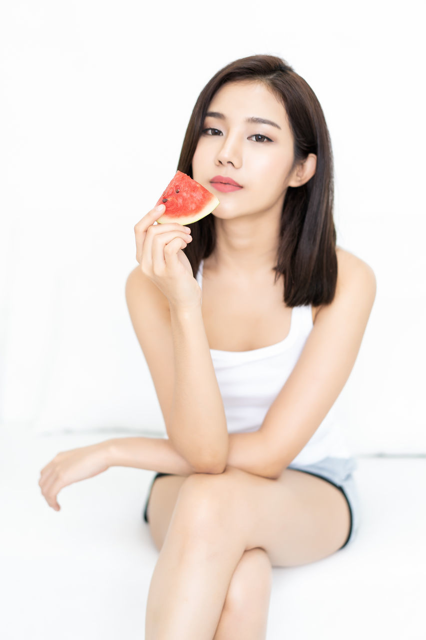 PORTRAIT OF A BEAUTIFUL YOUNG WOMAN SITTING ON WHITE BACKGROUND