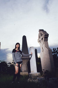 Young woman standing on cemetery against sky