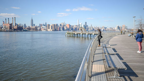 People standing on promenade by river against sky