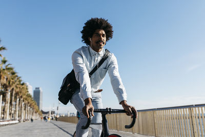 Mid adult man riding bicykle on a beach promenade, listening music