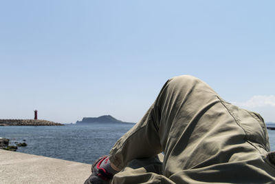 Low section of man sitting on shore against clear sky