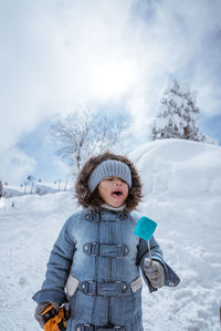 Portrait of young woman standing on snow covered field against sky