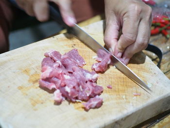 Cropped hand of woman cutting meat with table knife on cutting board