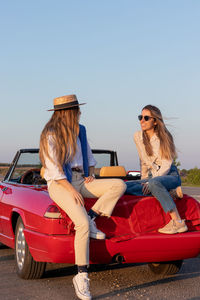 Portrait of young woman sitting on car against clear sky