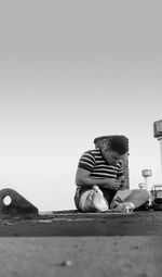 Man sitting on smart phone against clear sky