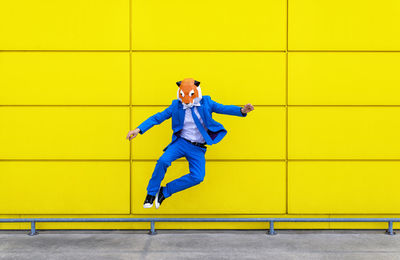 Portrait of man jumping against yellow wall