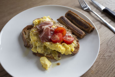 Close up of fresh scrambled eggs on toast with tomato and sausages