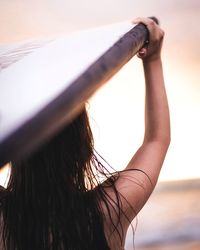 Rear view of woman carrying paddle board during sunset