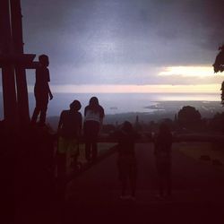 Silhouette people standing by sea against sky during sunset