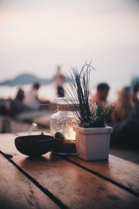 Glass jar by potted plant and bowl on table at beach during sunset