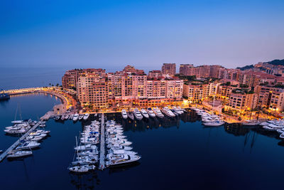 Sailboats in city by sea against clear blue sky