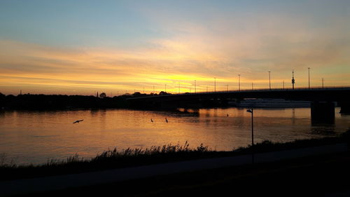 Silhouette bridge over river against sky at sunset