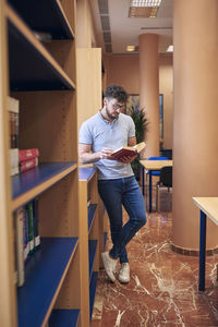 A boy is standing in a library looking at a book