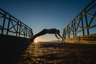 Man on bridge against clear sky during sunset