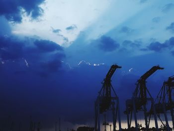 Silhouette cranes against sky