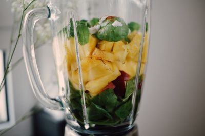 Close-up of fruit and herbs in blender against wall