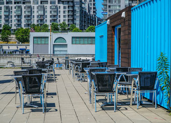 Empty chairs and tables at sidewalk cafe against buildings in city