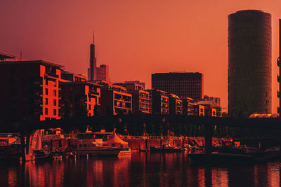 Illuminated buildings by river against sky during sunset