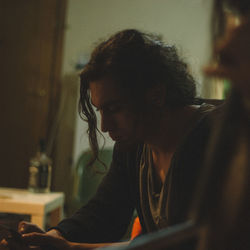 Close-up of young man with long hair using mobile phone at home