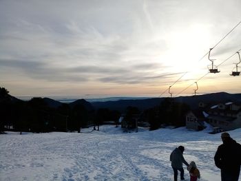 People on snow covered field against sky during sunset
