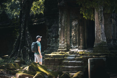 Traveler in cambodia. man with backpack admiring ancient temple ruins overgrown.