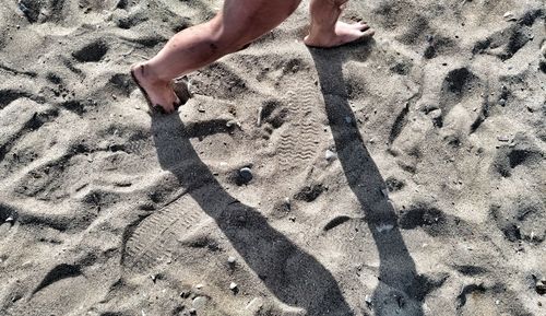 Low section of man on sand at beach during sunny day