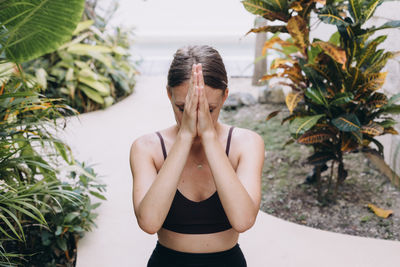 Young woman with hands folded in front of her face surrounded by lush foliage