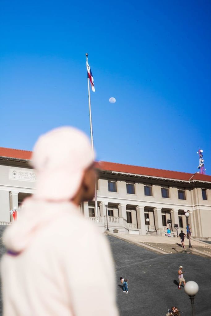 architecture, flag, building exterior, built structure, sky, blue, adult, men, clear sky, patriotism, city, day, rear view, nature, focus on background, sunny, government, travel destinations, outdoors, motion, group of people