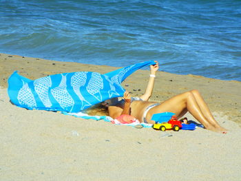 Young woman covering face with scarf while relaxing at beach