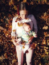 High angle view of baby boy lying on mother against autumn leaves