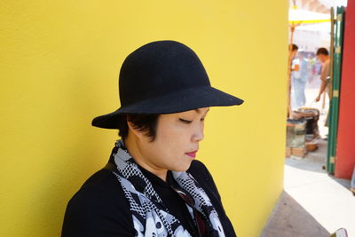 Close-up of mature woman wearing hat against yellow wall