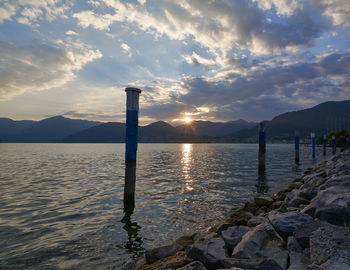 Wooden posts in river against cloudy sky