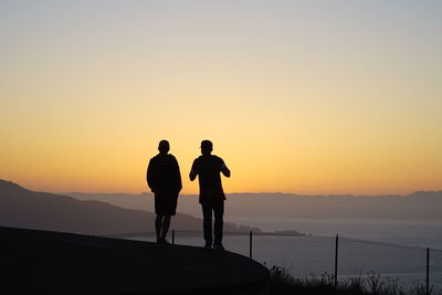 Silhouette men standing on mountain against sky during sunset