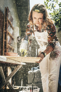 Female artist cutting wooden plank while working at backyard