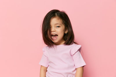 Portrait of young woman standing against pink background