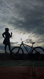 Silhouette man standing on bicycle against sky during sunset