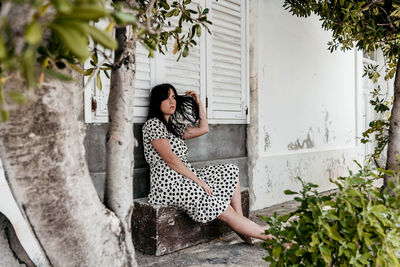 Beautiful young woman sitting on stone bench in front of old white house.